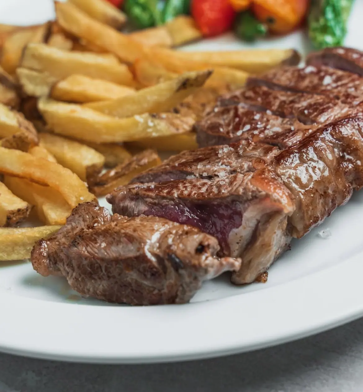 Carne a la parrilla cortada en tiras con sal en escamas, papas fritas y pimientos asados