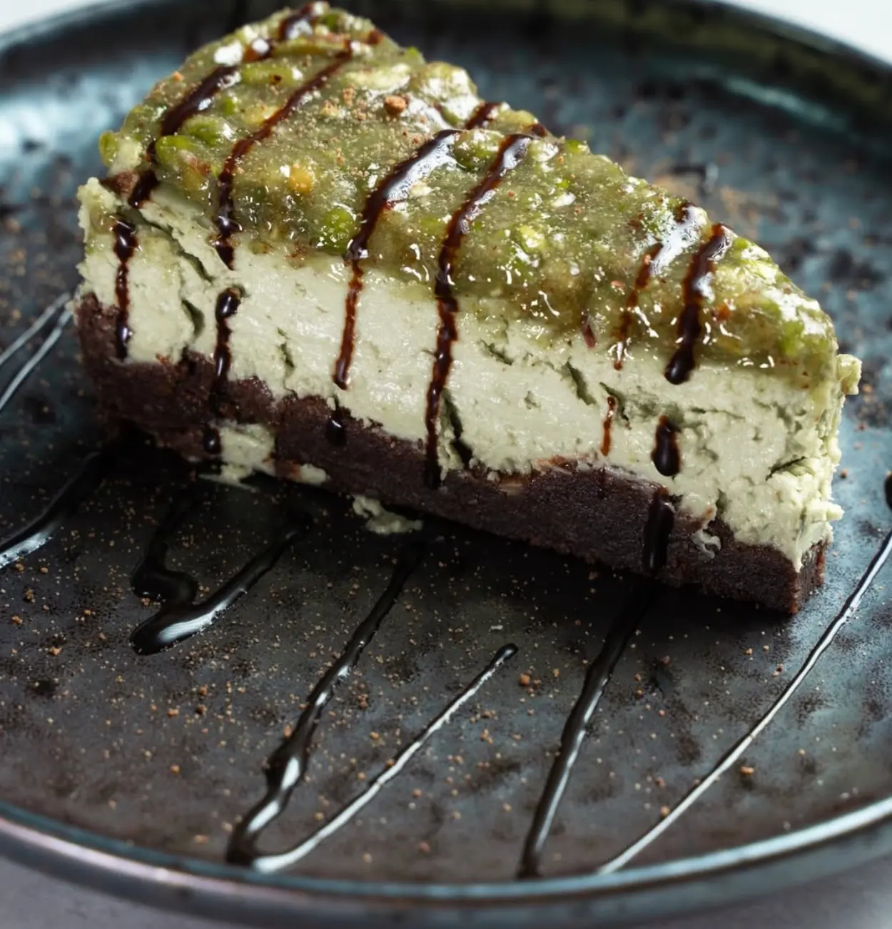 Porción de tarta de pistacho con base de chocolate e hilos de sirope oscuro
